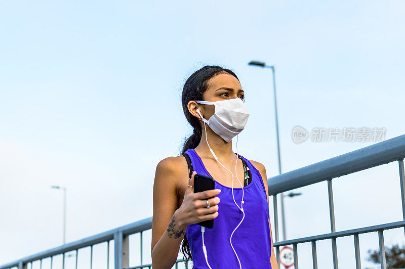 一个年轻的女人在新的常态下使用手机和耳机