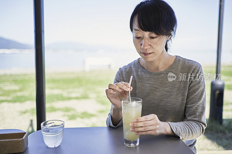 一位日本妇女在一家咖啡馆的露台上用可重复使用的吸管喝果汁。