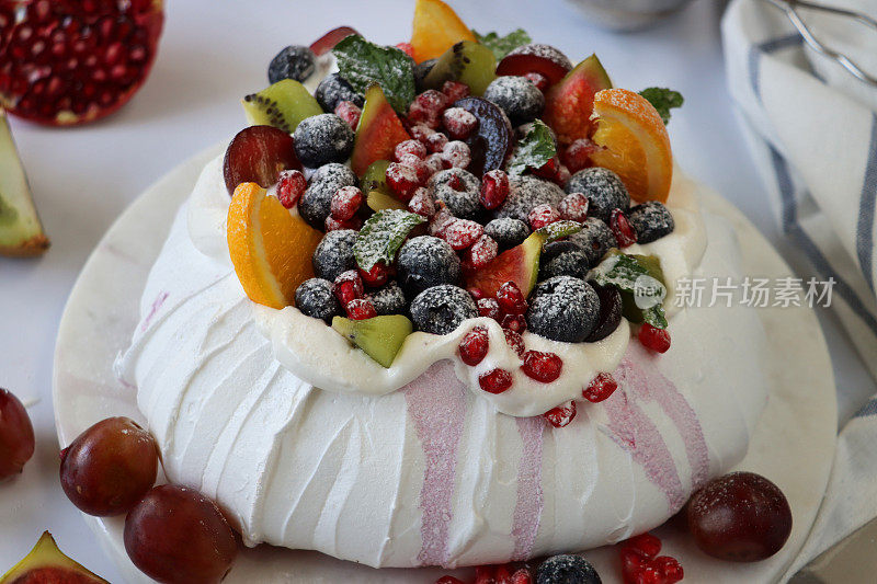 大理石蛋糕架上，大理石效果的背景，聚焦前景，用新鲜的水果，包括橙子，石榴籽，蓝莓，葡萄，猕猴桃和无花果撒上糖霜
