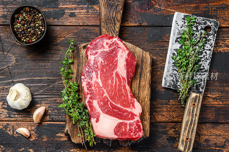 生黑安格斯上等牛肉卷牛排在切板与切肉刀。深色木制背景。俯视图