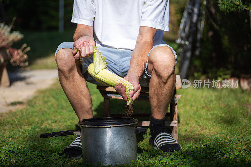 一名男子在室外的院子里剥新鲜的甜玉米