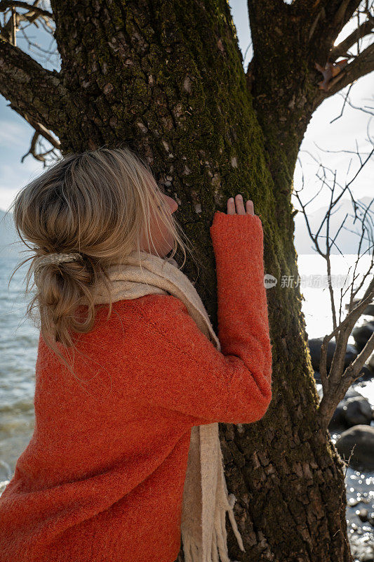 橙色套头衫的女子拥抱树干，热爱大自然