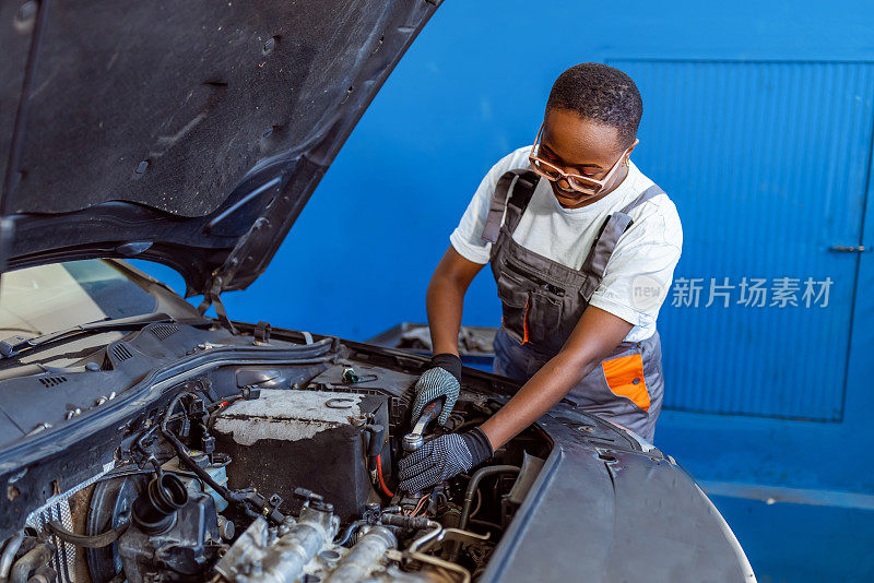 黑人女机械师在修车厂的引擎盖下工作。