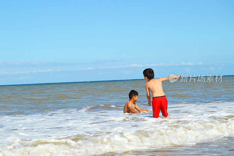 夏天的一天，两个孩子在海滩上的海浪中玩耍