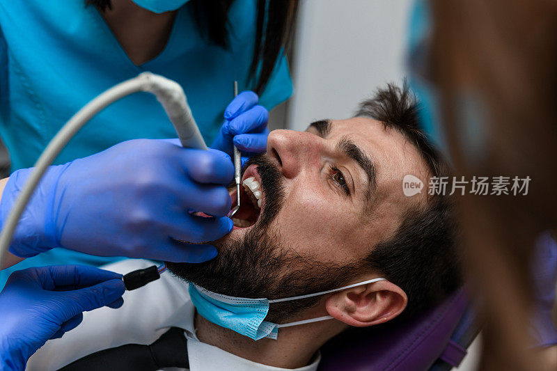 在牙科诊所里，一位戴着蓝手套的牙医正在给一个年轻人钻牙