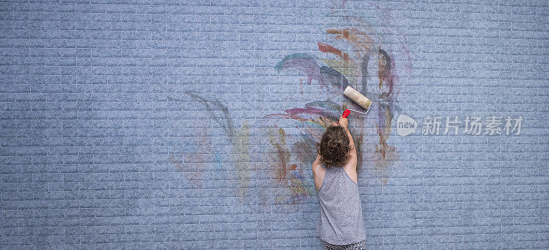 一个6岁的白人女孩在墙上画画。小女孩手里拿着一个油漆滚筒。