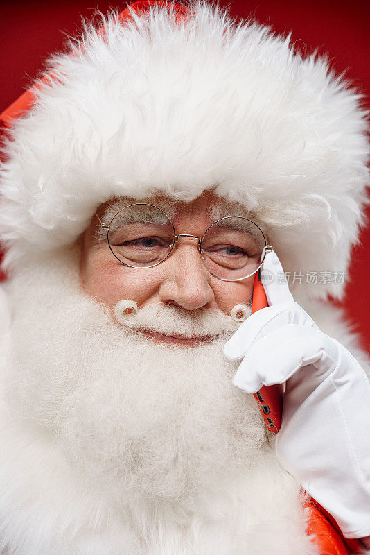 一个微笑的圣诞老人在红色背景下用他的红色智能手机说话的特写