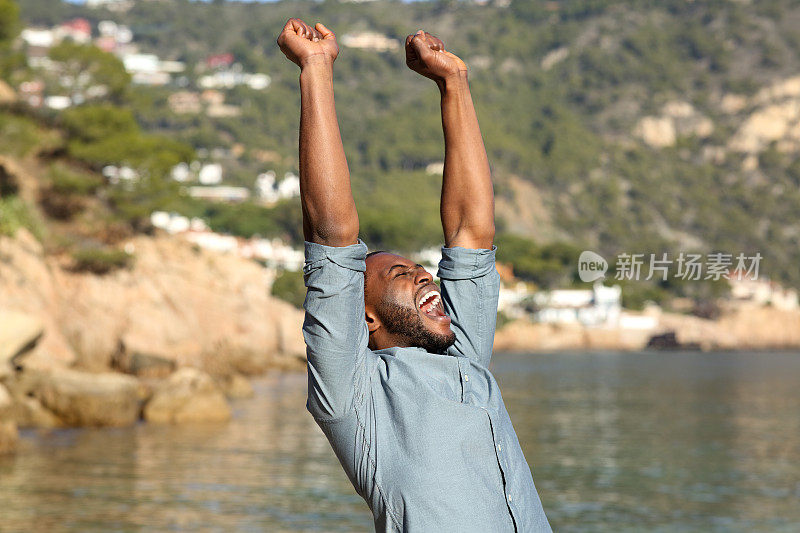一个黑皮肤的男人在海滩上举起手臂庆祝