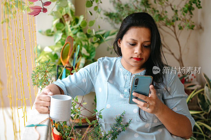 在阳台上用智能手机和拿着一杯茶或咖啡的年轻女子。