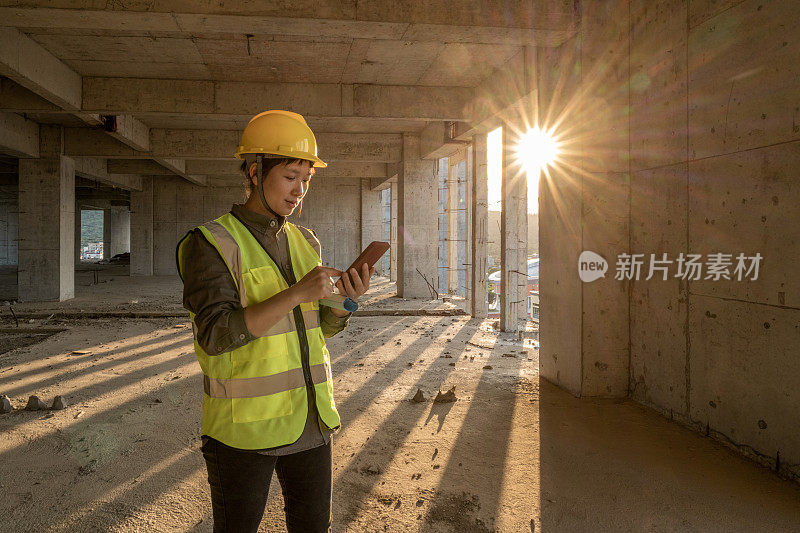 一位亚洲女建筑工人正在工地上使用手机