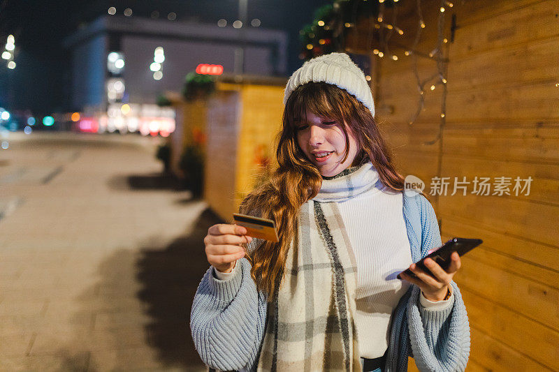 微笑的年轻女子手持信用卡和智能手机在网上购物