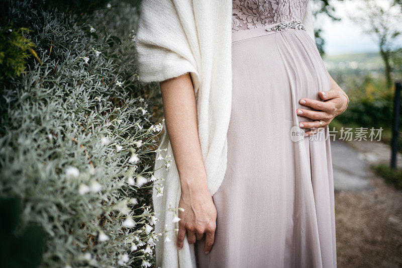 穿着淡紫色的裙子，手放在孕妇的肚子上