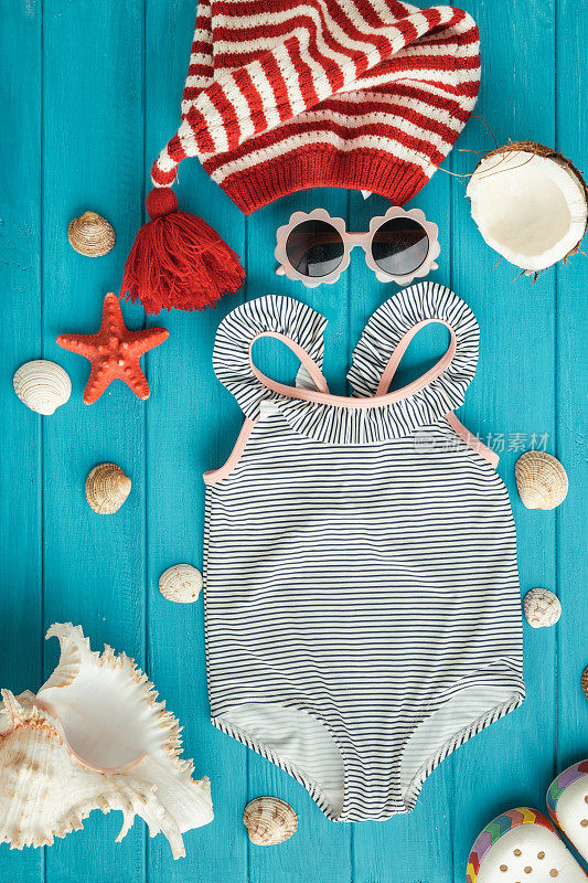 泳衣和圣诞帽旁边的海滩配件被贝壳包围，海星上的木制蓝绿色背景。夏天的氛围在冬季和圣诞假期的海边概念