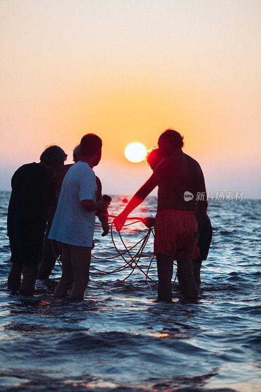 日落时分，朋友们在海滩上用网钓鱼
