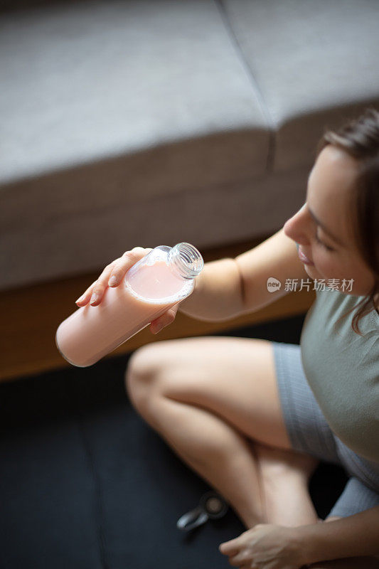 年轻女子在家里的客厅锻炼期间补水。