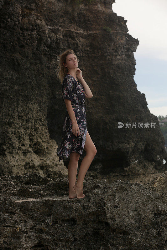 美丽的年轻女子在黑色花裹裙的肖像野生岩石海滩