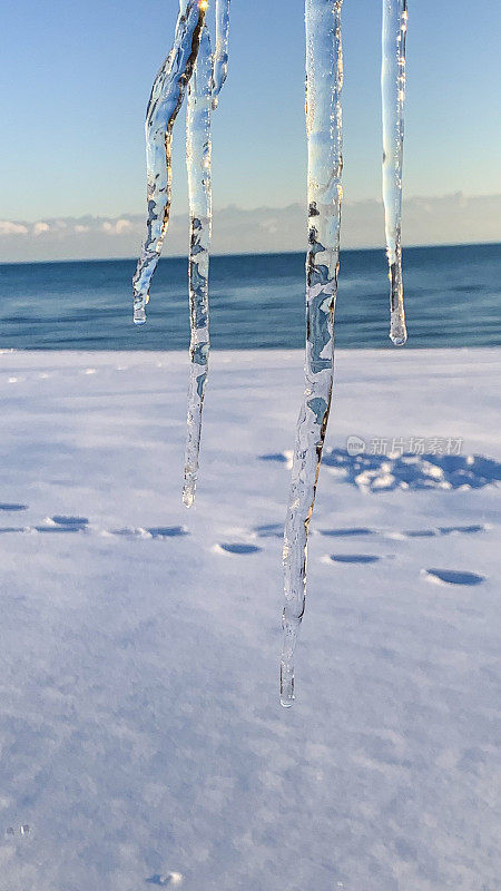 冰柱在阳光下悬挂下来，特写在雪地沙滩上的脚印