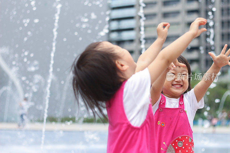 一对亚洲双胞胎女孩在喷泉前玩水
