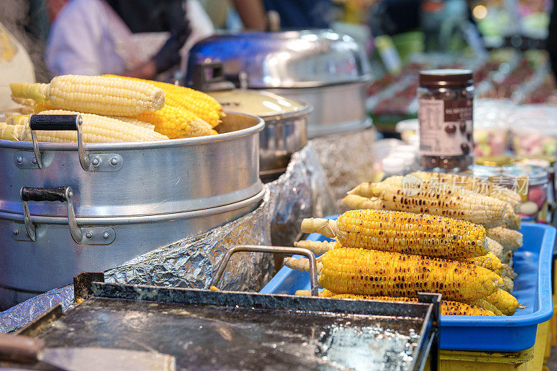 在一个特写镜头中，蒸熟和烤熟的甜玉米放在一个托盘上，准备在亚洲夜市出售