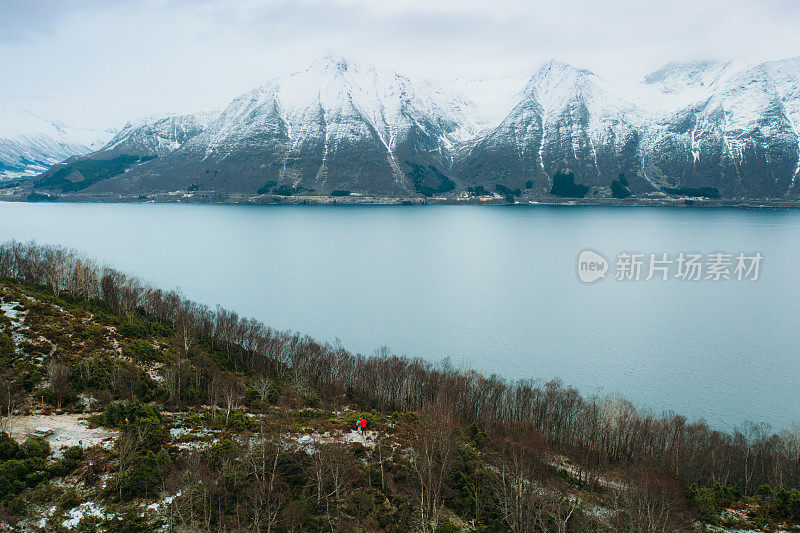 鸟瞰图:女人和男人带着狗呆在山顶上欣赏挪威冬季峡湾的风景