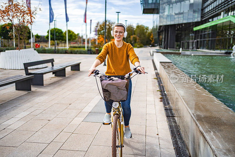 一头短发的白人女子在城市里骑自行车时戴着无线耳机听音乐