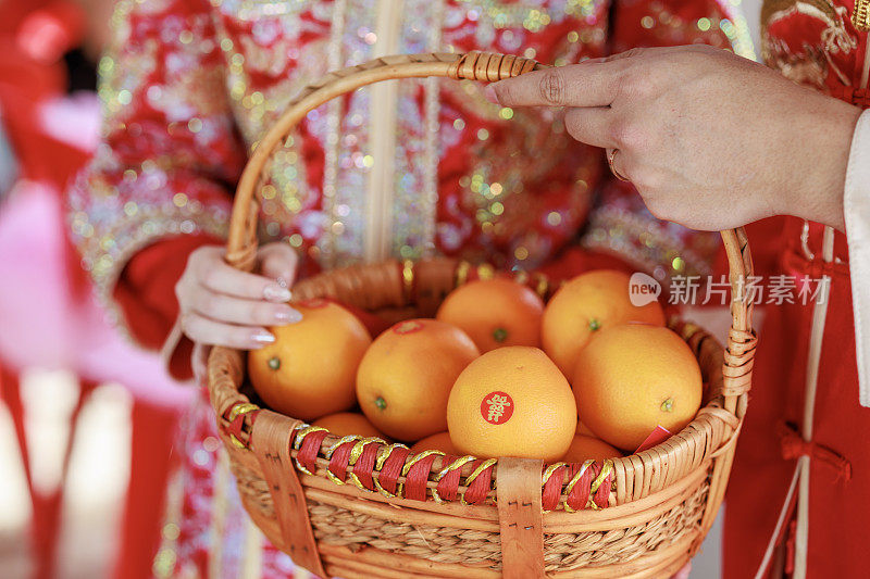 一对新婚夫妇手持中国传统的结婚篮子，篮子上的新鲜橙子上有“双喜”的标志。