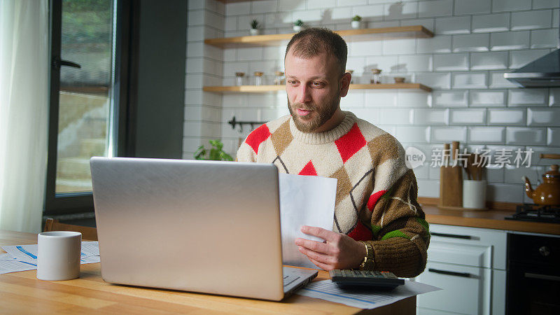 成年男人坐在厨房用笔记本电脑支付账单，用计算器计算费用，做预算控制，管理财务，审查逾期贷款