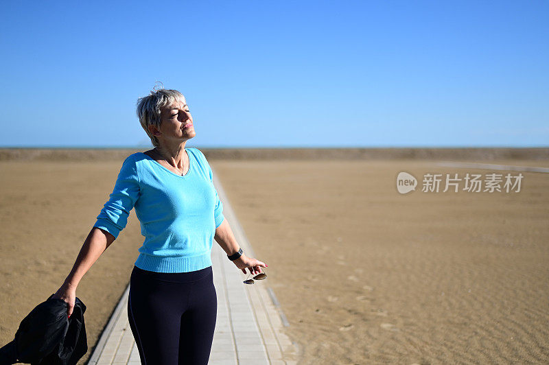 在温暖的春天，一位年长的女性在海滩上呼吸着新鲜的空气。