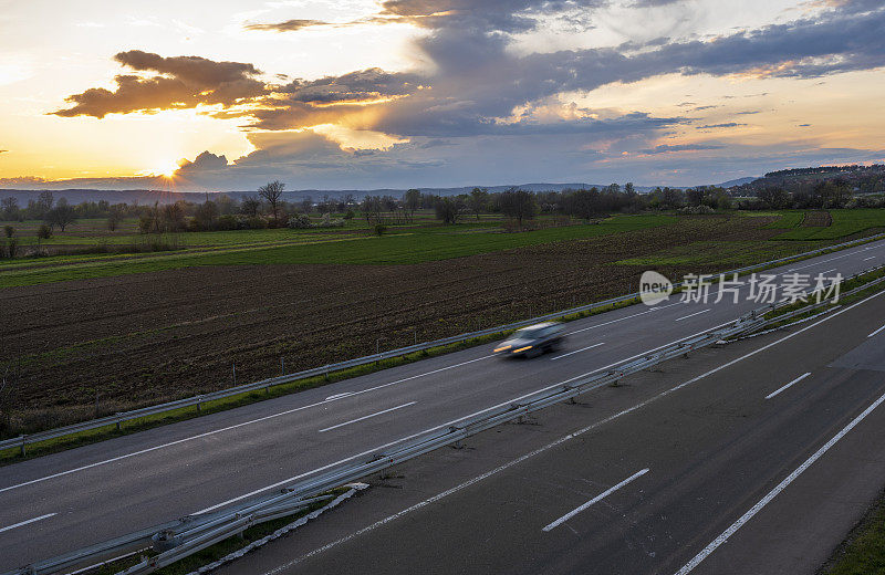 汽车在公路上高速行驶，穿过乡村风景。高速公路高速行驶。高速公路上超速行驶的景象。背景是美丽的日落。