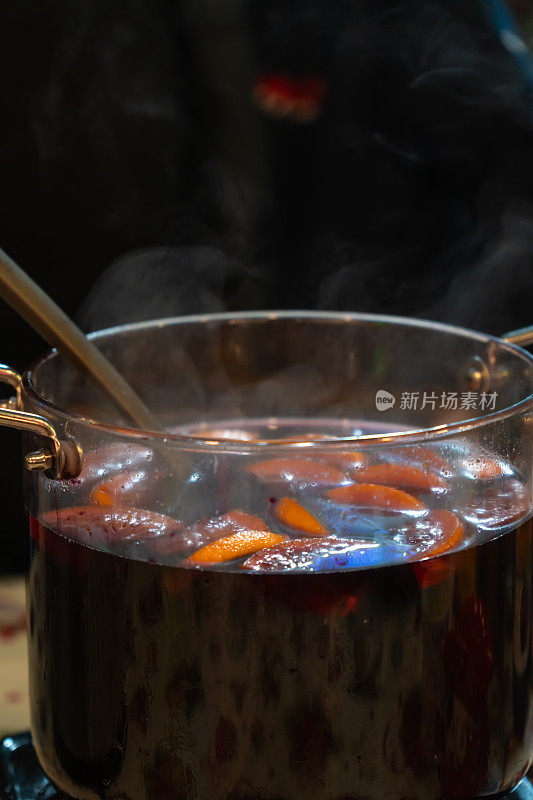 户外集市和节日上，一个大玻璃锅里盛着由水果和浆果制成的辛辣热酒。垂直图