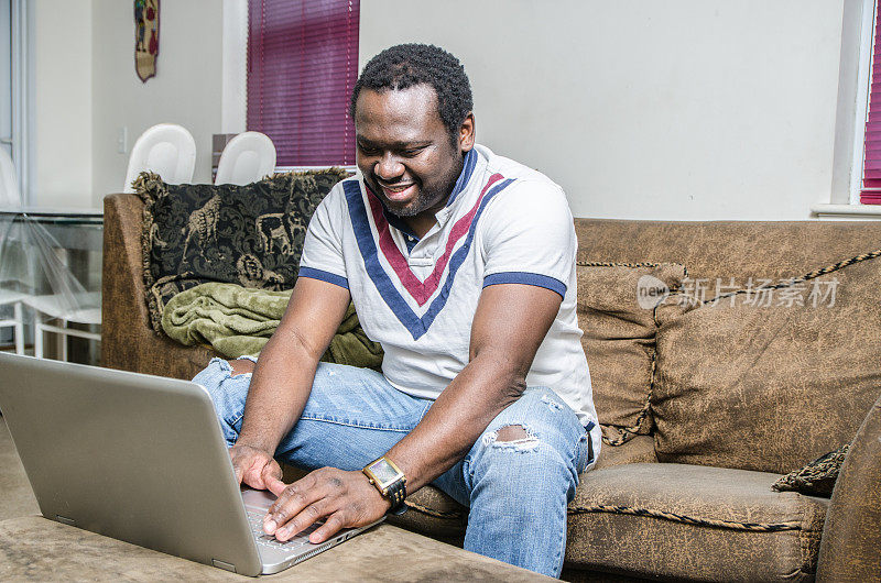 一个年轻的黑人坐在沙发上使用笔记本电脑
