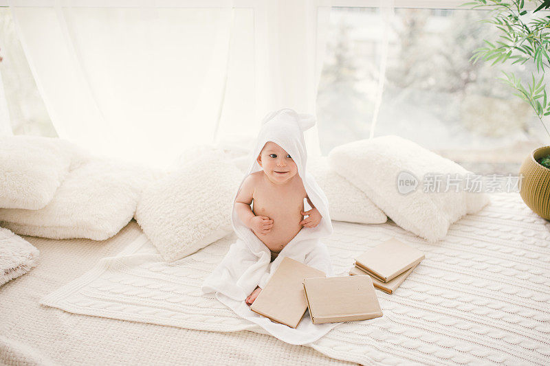 在一扇大窗的背景下，一个孩子坐在一条编织的毯子上，戴着白色的竹毛巾，耳朵。
