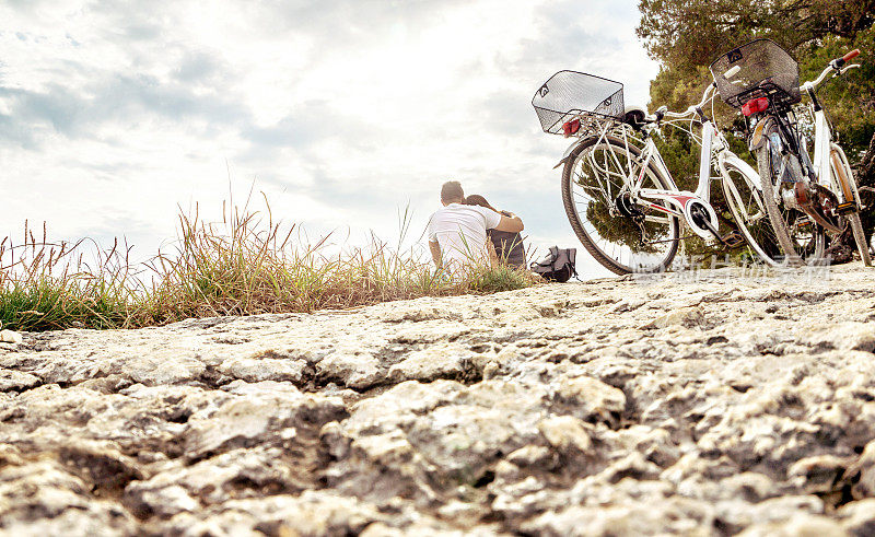 一对自行车旅行的夫妇。情侣们坐在海边的沙滩、岩石、悬崖或森林里。在骑车休息时停放的自行车。