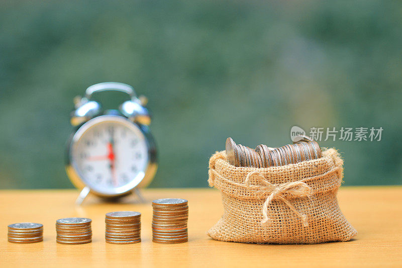 金融，在自然绿色的背景下，一堆硬币钱在袋子里，闹钟，商业投资和存钱准备未来的概念