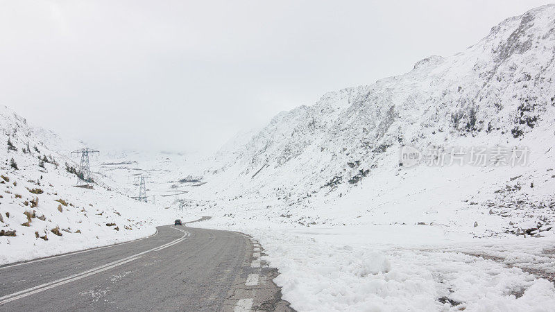 一辆黑色轿车在雪山之间的发夹弯道上行驶