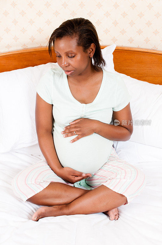 一名孕妇在床上摸着自己的肚子