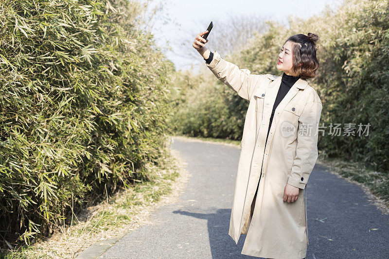 一名女子在公园小径上用智能手机拍照