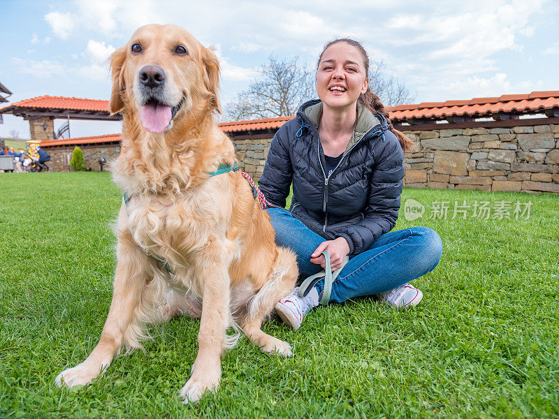 年轻的女人和她的金毛猎犬坐在户外看相机