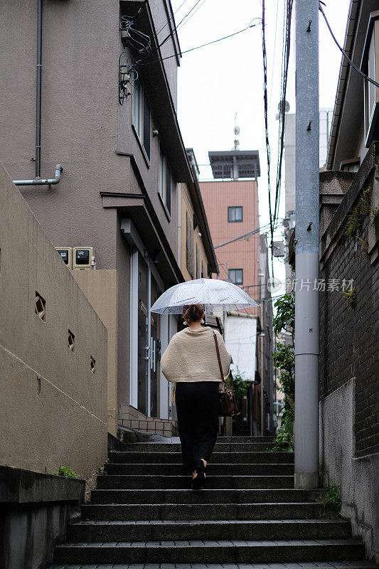 一名妇女走在东京神乐坂传统老城的小巷里，在一个雨天