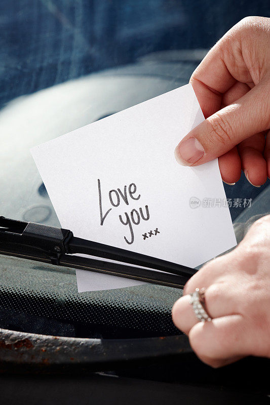 手把写有“爱你”的纸条塞在汽车挡风玻璃的刮水器下
