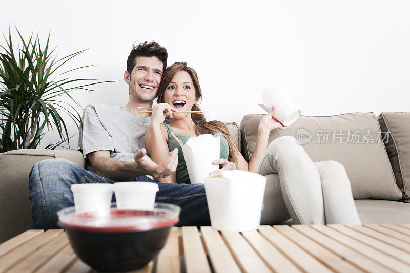 年轻夫妇一边吃中餐一边看电视。