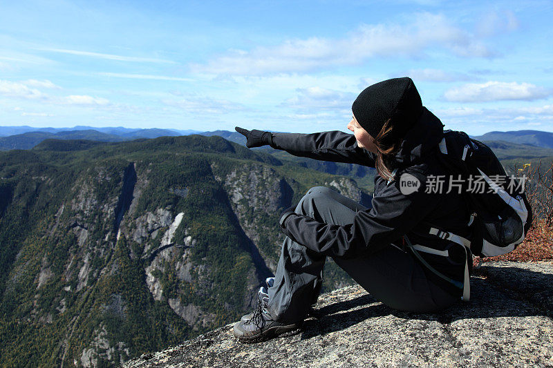 女性徒步旅行者坐在山顶，指向一个方向