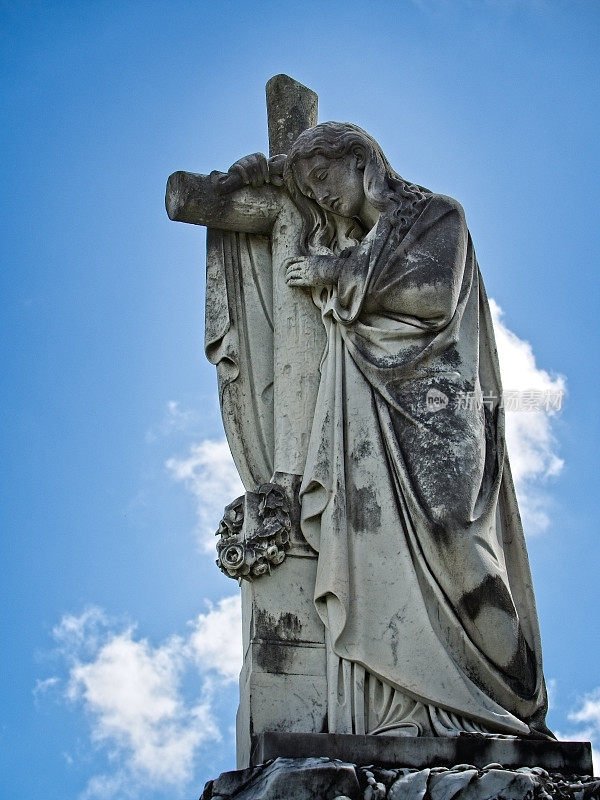 一个女人在坟墓上举着十字架的雕像