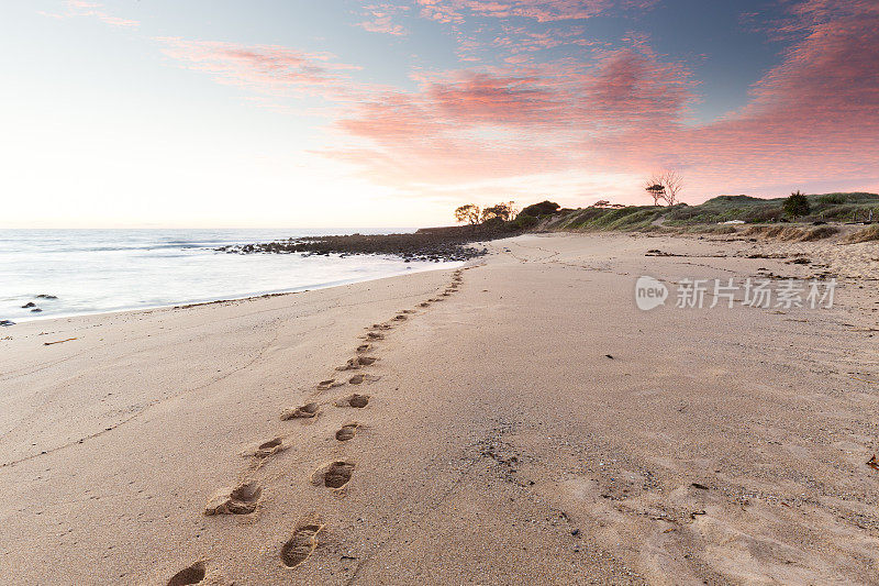 沙滩脚印通向一个粉红色的日出