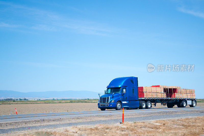 大卡车蓝色半挂车与平床拖车运输木材木材在平坦的道路上