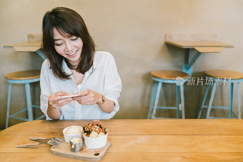 美丽的亚洲女孩拍照的巧克力吐司蛋糕，冰淇淋，和牛奶在咖啡店。甜点或食物摄影爱好。智能手机或手机拍照习惯概念。与复制空间