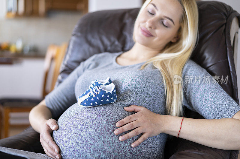 怀孕的长女人睡在沙发上，宝宝的鞋子放在肚子上