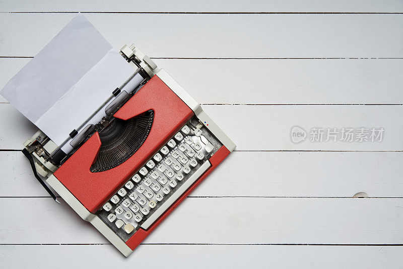 红色老式打字机，白色木桌上有白纸
