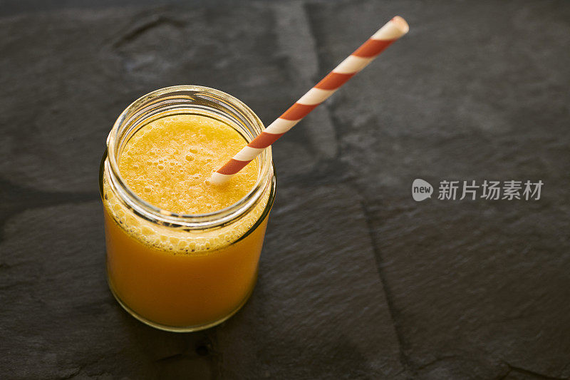 盛满新鲜橙汁的玻璃瓶，用稻草铺在石板背景上。