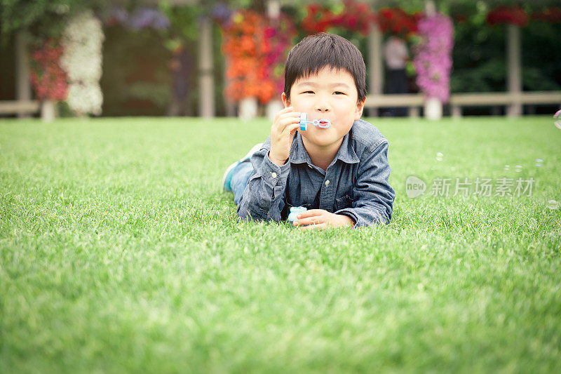 快乐的亚洲小男孩在草地上吹泡泡